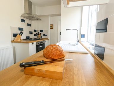 A kitchen countertop with a loaf of bread and a knife near a sink and stove at Lime Cottage in Burton Bradstock