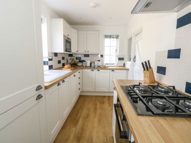 A kitchen with wooden countertops a gas stove a knife block and white cabinets at Lime Cottage in Burton Bradstock