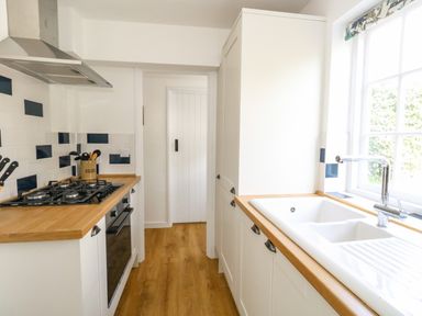 A kitchen with a gas stove oven wooden countertops white cabinets and a window above the sink at Lime Cottage in Burton Bradstock