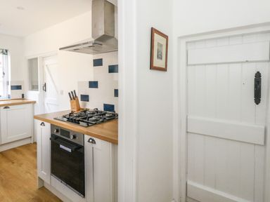 A kitchen with a gas stove oven wooden countertops white cabinets and a white door with black handle at Lime Cottage in Burton Bradstock