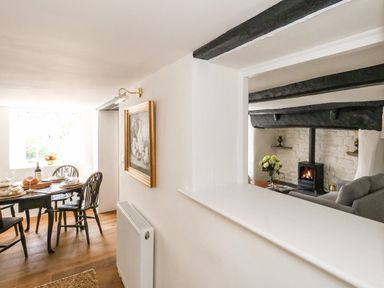 A dining area with a table set for four and a living room with a wood stove and exposed beams at Lime Cottage in Burton Bradstock