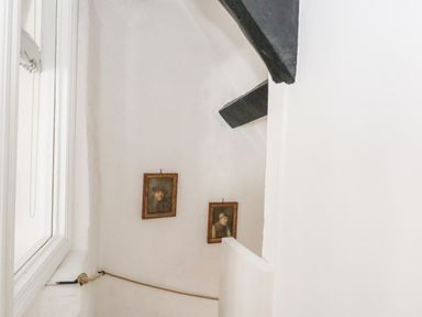 A stairway with two framed portraits on white walls and a window to the side at Lime Cottage in Burton Bradstock