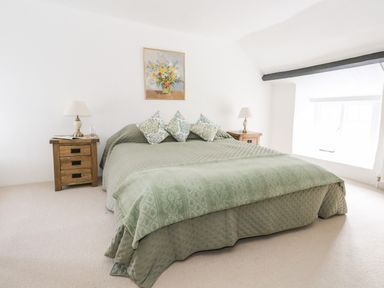 A bedroom with a bed covered in green bedding and floral pillows alongside wooden nightstands with lamps at Lime Cottage in Burton Bradstock