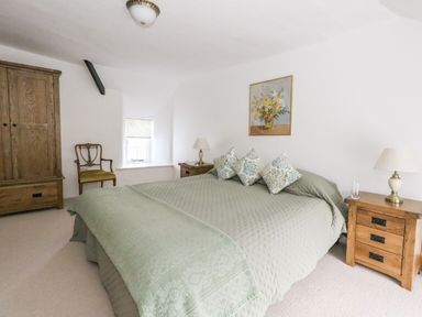 A bedroom with a large bed with green bedding wooden nightstands with lamps a wooden wardrobe and a chair at Lime Cottage in Burton Bradstock