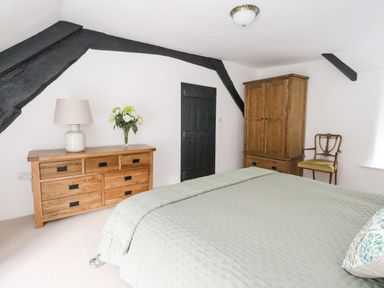 A bedroom with a bed covered in a pale green quilt and pillow a wooden dresser with a lamp and flowers a wooden wardrobe and a wooden chair at Lime Cottage in Burton Bradstock