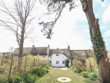 A garden with grass and plants bordered by wooden lattice fences in front of thatched roof cottages at Lime Cottage in Burton Bradstock