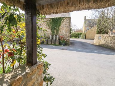 A view of a street with stone buildings plants and milk churns at Lime Cottage in Burton Bradstock