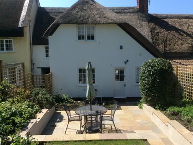 A garden patio area with a round table and four chairs in front of a thatched roof house at Lime Cottage in Burton Bradstock
