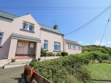 A row of pink houses with windows and doors next to green bushes and a clear blue sky at 2 Sunny Hill in Porthgain near St Davids