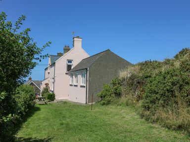 Exterior side view of houses with grass lawn and bushes under a clear blue sky at 2 Sunny Hill in Porthgain near St Davids