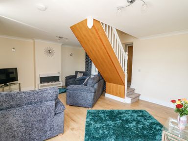 A living room with grey sofas a TV a fireplace blue rugs and a staircase at 2 Sunny Hill in Porthgain near St Davids