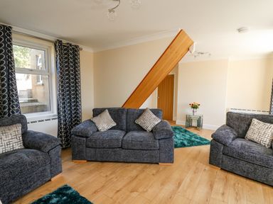 A living room with three dark gray sofas two rugs a glass side table with flowers and blue patterned curtains at 2 Sunny Hill in Porthgain near St Davids