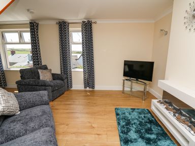 A living room with two dark sofas a television on a glass stand a wall-mounted fireplace and a blue rug at 2 Sunny Hill in Porthgain near St Davids