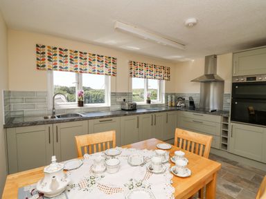 A kitchen with a wooden table set for tea and green cabinets at 2 Sunny Hill in Porthgain near St Davids