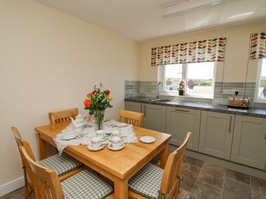 A kitchen with a wooden dining table set with tea cups flowers and a sink under a window at 2 Sunny Hill in Porthgain near St Davids