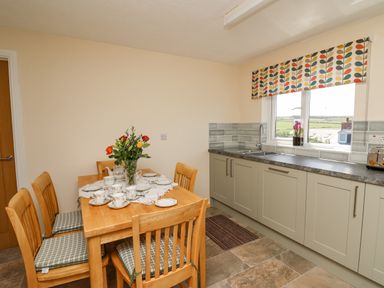 A kitchen with wooden dining table and chairs with teacups and flowers and countertop with sink and window at 2 Sunny Hill in Porthgain near St Davids