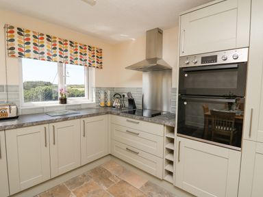 A kitchen with cabinets a countertop stove oven toaster and a window with a patterned blind at 2 Sunny Hill in Porthgain near St Davids