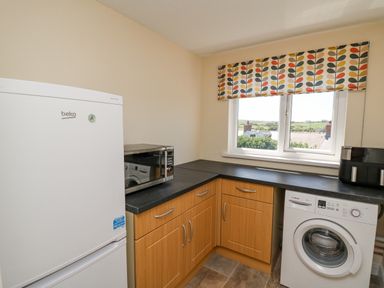 A kitchen with a fridge freezer microwave washing machine and a window with a patterned blind at 2 Sunny Hill in Porthgain near St Davids