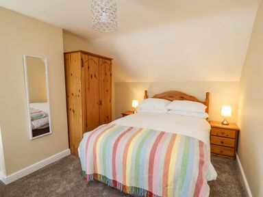 A bedroom with a double bed covered with a striped blanket two bedside tables with lamps a wooden wardrobe and a wall mirror at 2 Sunny Hill in Porthgain near St Davids