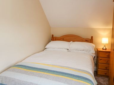 A bedroom with a wooden bed white bedding a striped blanket a wooden nightstand with a lamp at 2 Sunny Hill in Porthgain near St Davids