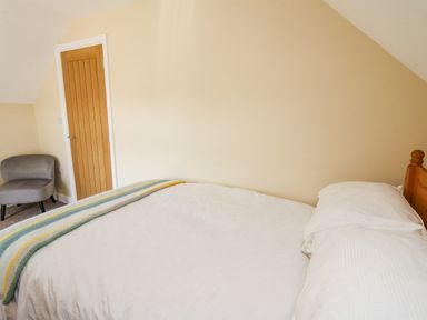 A bedroom with a wooden door grey chair and a bed with white bedding at 2 Sunny Hill in Porthgain near St Davids