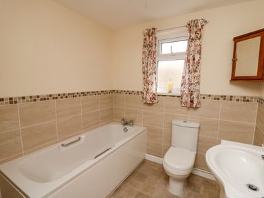 A bathroom with a bathtub toilet sink floral curtains and a wooden mirror cabinet at 2 Sunny Hill in Porthgain near St Davids