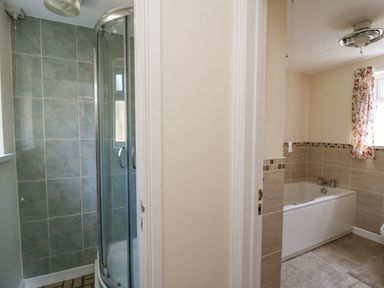 A bathroom with a shower enclosure on the left and a bathtub with tiled walls on the right at 2 Sunny Hill in Porthgain near St Davids