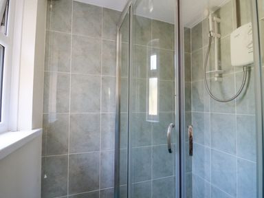 A tiled shower enclosure with glass doors and an electric shower unit at 2 Sunny Hill in Porthgain near St Davids