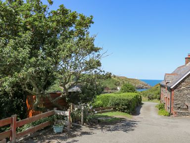 A country road with a stone house and green hedges leading to the sea at 2 Sunny Hill in Porthgain near St Davids