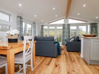 A living room with gray sofas wooden dining table and chairs and large windows with curtains at 7 Valley View in Lanreath
