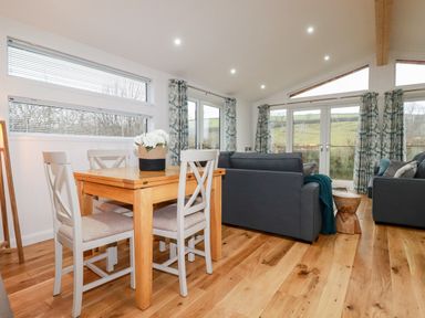 A dining table with four chairs and a flower pot next to two sofas in a room with large windows at 7 Valley View in Lanreath