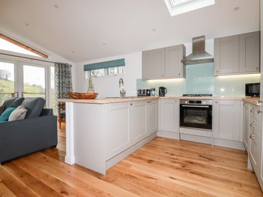 A kitchen with light gray cabinets wooden floors and a sofa near glass doors at 7 Valley View Lanreath