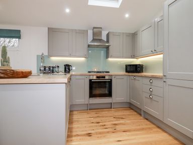 A kitchen with wooden floors grey cabinets a stove microwave and countertop appliances at 7 Valley View in Lanreath