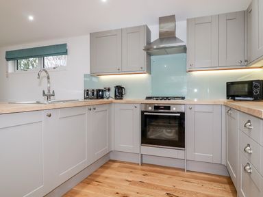 A kitchen with grey cabinets wooden countertops a built-in oven stovetop microwave toaster kettle and a window at 7 Valley View in Lanreath