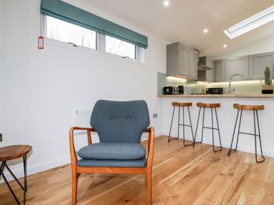 A chair with wooden arms and blue cushions near a kitchen counter with three bar stools and appliances at 7 Valley View in Lanreath