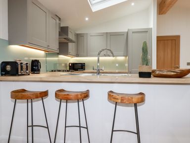 A kitchen with three wooden bar stools a countertop with a sink a cactus plant a toaster kettle microwave and grey cabinets at 7 Valley View in Lanreath
