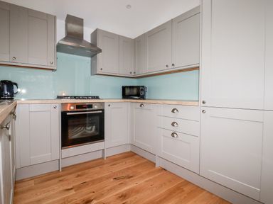 A kitchen with gray cabinets wooden counters a stainless steel oven stove hood a microwave and a black kettle at 7 Valley View in Lanreath