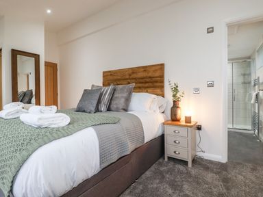 A bedroom with a bed with pillows and folded towels next to a nightstand and an open door showing a bathroom at 7 Valley View in Lanreath