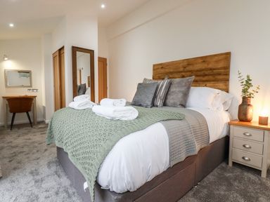 A bedroom with a bed with pillows and folded towels a nightstand with a vase and a lamp a desk with a chair and a mirror at 7 Valley View in Lanreath