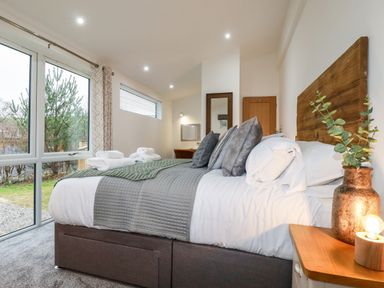 A bedroom with a bed with grey bedding and pillows next to a bedside table with a lamp and plant at 7 Valley View in Lanreath