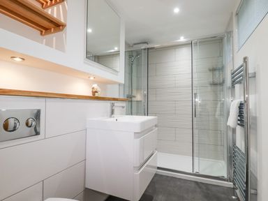A bathroom with a shower enclosure, a white sink cabinet, a mirror, a towel rail, and a wooden shelf at 7 Valley View in Lanreath