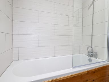 A bathtub with a glass shower screen and tiled walls at 7 Valley View in Lanreath
