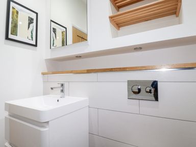 A bathroom sink with a faucet a mirror above a wooden shelf and a framed picture on the wall at 7 Valley View in Lanreath
