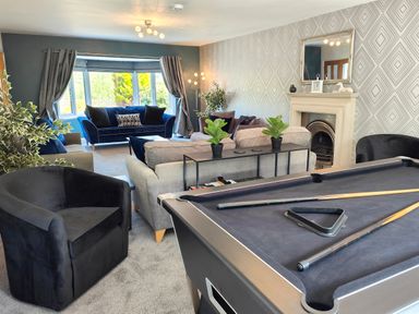 A living room with a pool table two armchairs two sofas plants a fireplace and large windows at Sanderson House in Cleator Moor