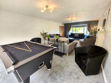 A living room with a pool table chairs sofas and a large window at Sanderson House in Cleator Moor