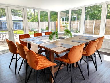 A dining room with a wooden table and orange chairs with windows overlooking a garden at Sanderson House in Cleator Moor