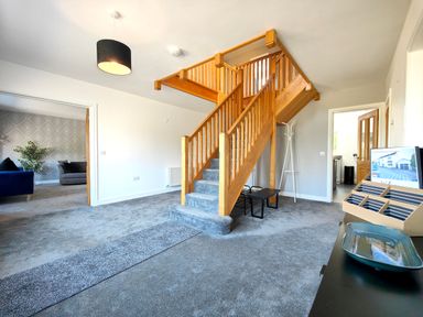 A hallway with wooden staircase and carpeted floor connected to a living room with sofas at Sanderson House in Cleator Moor