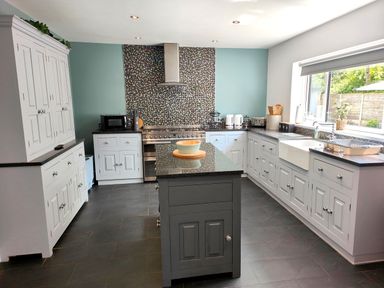 A kitchen with white cabinets a central island stove with mosaic backsplash and a large window at Sanderson House in Cleator Moor