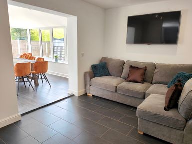 A living room with a gray sectional sofa and mounted flat screen tv next to a dining area with orange chairs at Sanderson House in Cleator Moor