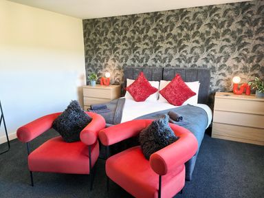 A bedroom with two red chairs and a double bed with red pillows at Sanderson House in Cleator Moor